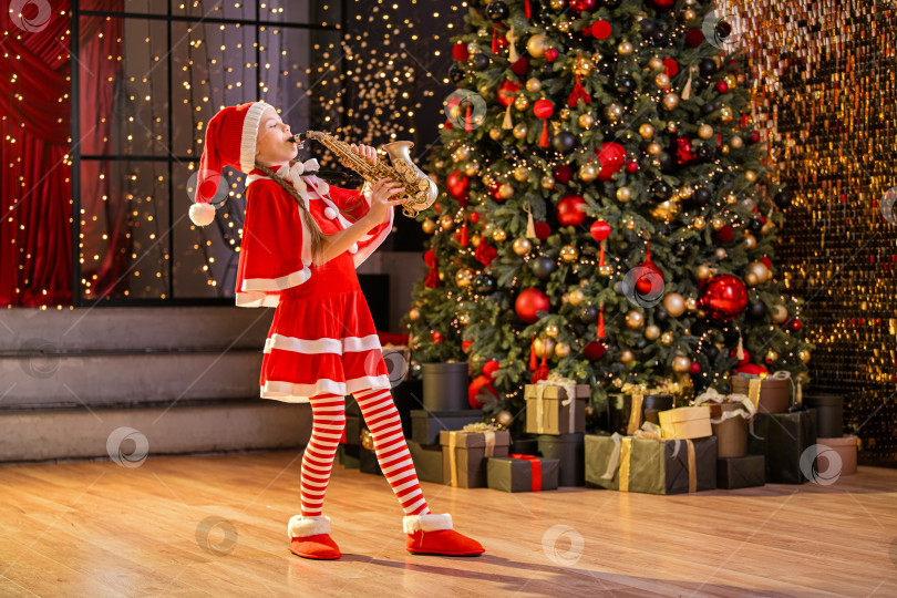 Скачать девушка в костюме Санта-Клауса играет на саксофоне возле рождественской елки фотосток Ozero