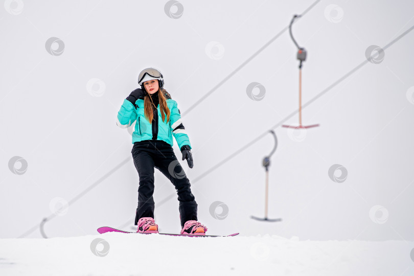 Скачать Молодая сноубордистка, скользящая по заснеженному склону в стильном зимнем снаряжении. Захватывающие зимние виды спорта. фотосток Ozero
