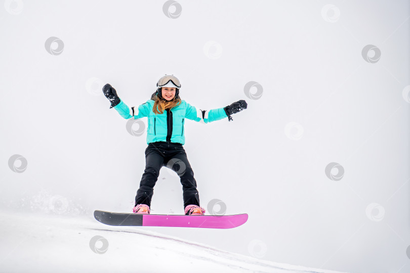 Скачать Молодая сноубордистка, скользящая по заснеженному склону в стильном зимнем снаряжении. Захватывающие зимние виды спорта. фотосток Ozero