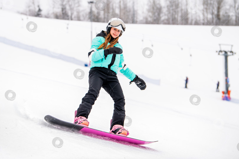 Скачать Молодая сноубордистка, скользящая по заснеженному склону в стильном зимнем снаряжении. Захватывающие зимние виды спорта. фотосток Ozero