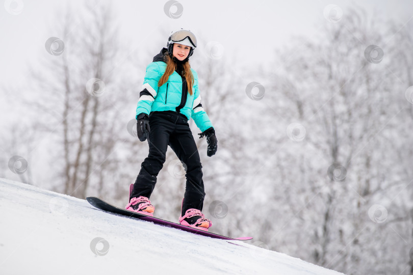 Скачать Молодая сноубордистка, скользящая по заснеженному склону в стильном зимнем снаряжении. Захватывающие зимние виды спорта. фотосток Ozero
