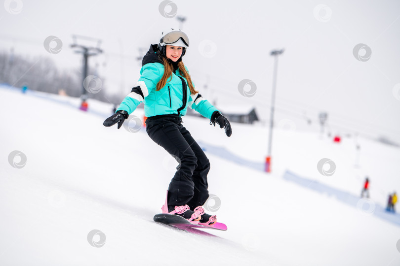 Скачать Молодая сноубордистка, скользящая по заснеженному склону в стильном зимнем снаряжении. Захватывающие зимние виды спорта. фотосток Ozero