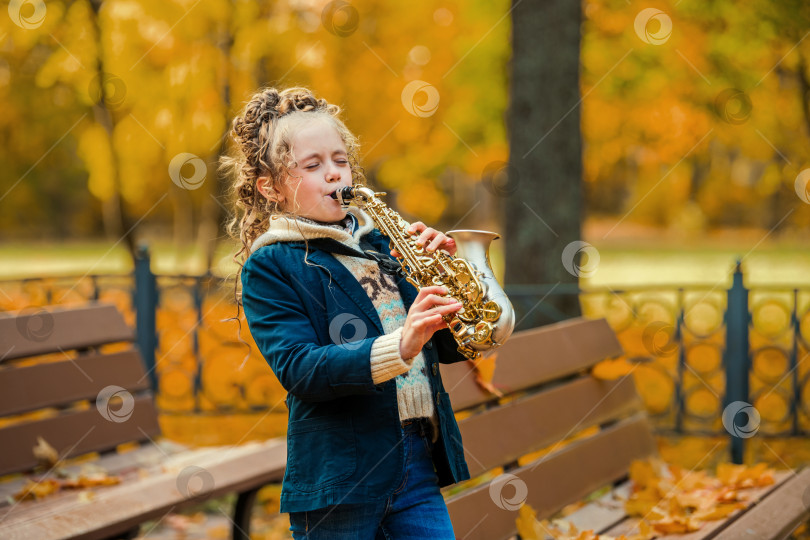 Скачать Маленькая девочка играет на саксофоне в осеннем парке в солнечный день. фотосток Ozero
