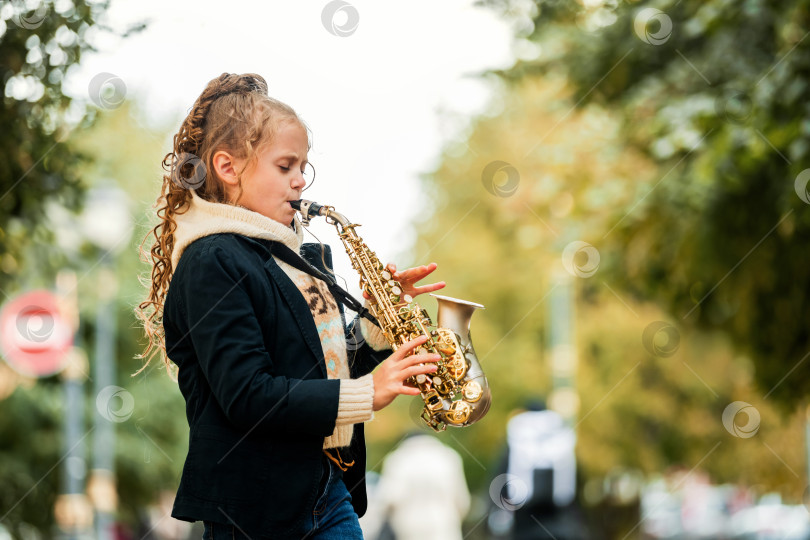 Скачать Молодая девушка играет на саксофоне во время выступления на открытом воздухе. фотосток Ozero
