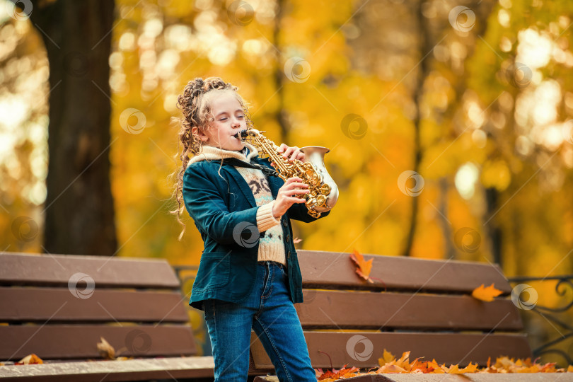 Скачать Маленькая девочка играет на саксофоне в осеннем парке в солнечный день. фотосток Ozero
