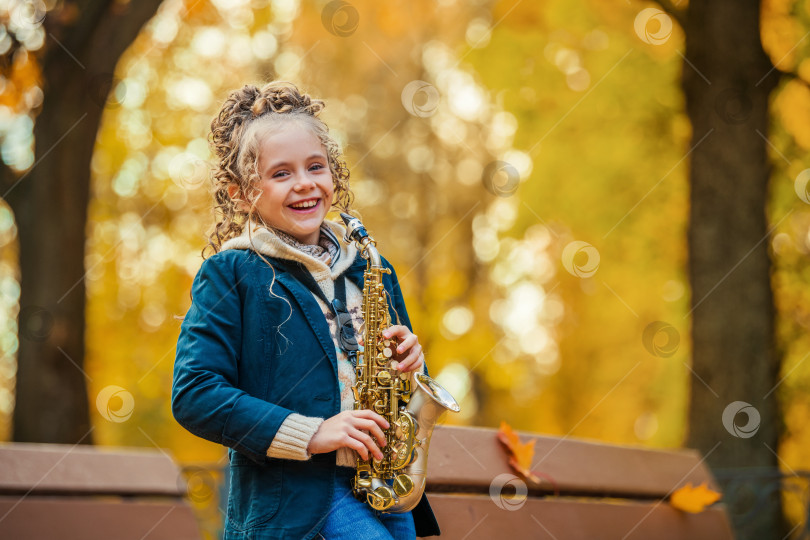 Скачать Счастливая молодая женщина играет на саксофоне на открытом воздухе прекрасным осенним днем. фотосток Ozero