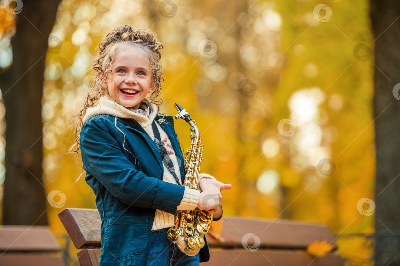 Скачать Молодая девушка стоит с саксофоном в осеннем парке. фотосток Ozero
