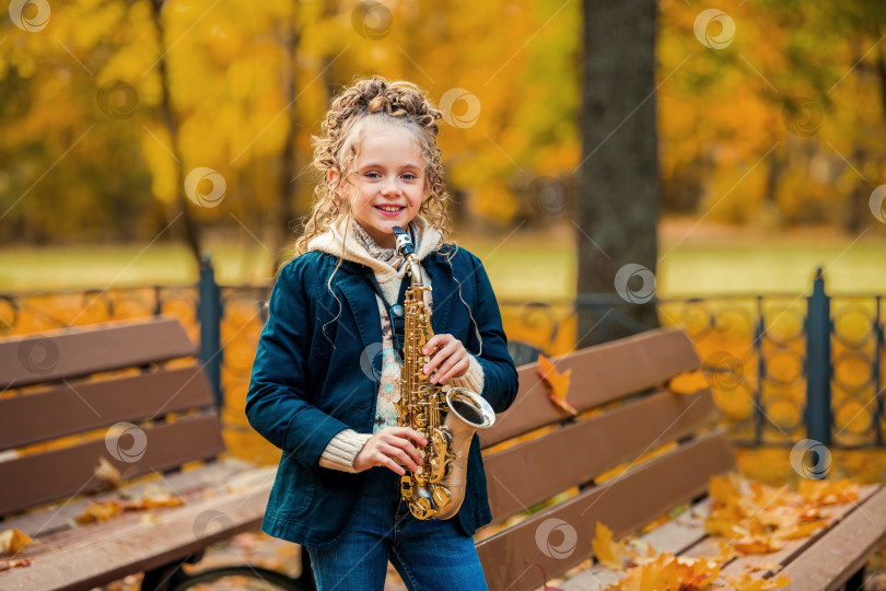 Скачать Молодая девушка стоит с саксофоном в осеннем парке. фотосток Ozero
