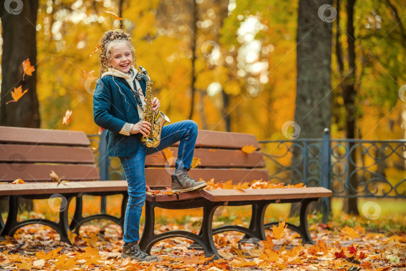 Скачать Маленькая девочка играет на саксофоне в осеннем парке. фотосток Ozero