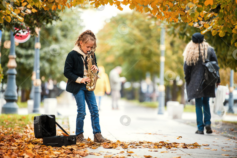 Скачать Молодая девушка играет на саксофоне на улице в окружении опавших осенних листьев. фотосток Ozero