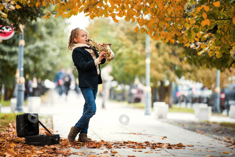 Скачать Молодая девушка играет на саксофоне на улице в окружении опавших осенних листьев. фотосток Ozero