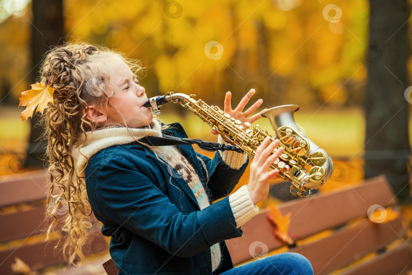 Скачать Маленькая девочка играет на саксофоне в осеннем парке в солнечный день. фотосток Ozero
