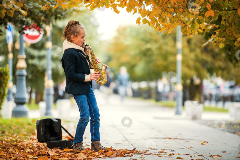 Скачать Молодая девушка играет на саксофоне на улице в окружении опавших осенних листьев. фотосток Ozero
