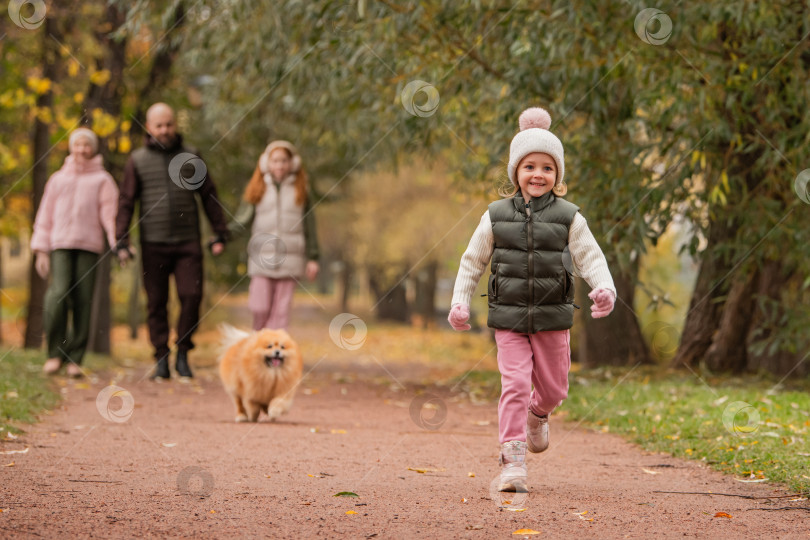 Скачать маленькая девочка и ее домашний шпиц бегут по дорожке в осеннем городском парке. фотосток Ozero