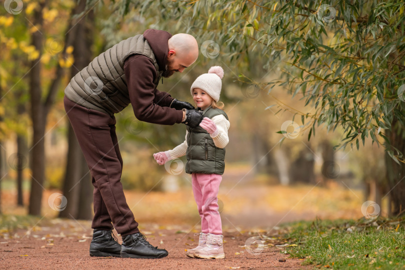 Скачать счастливый отец тщательно застегивает молнию на куртке своей маленькой дочери во время прогулки по осеннему парку. фотосток Ozero