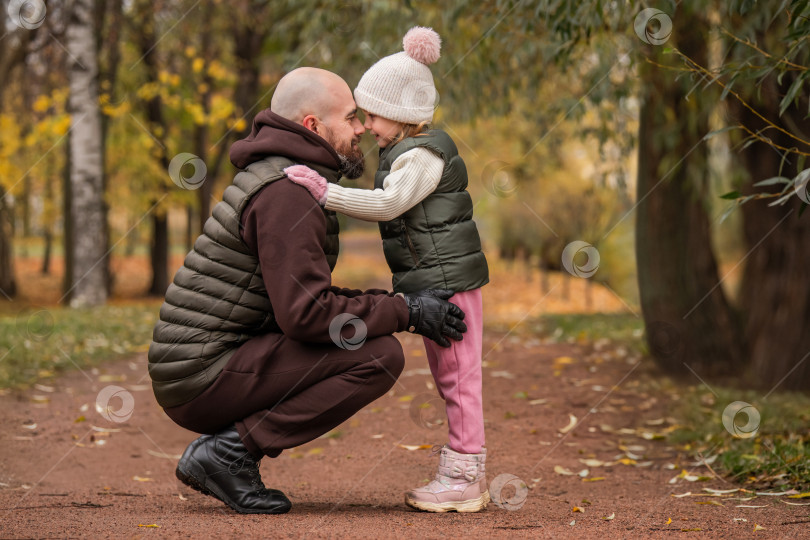 Скачать Маленькая дочь обнимает своего любящего отца во время прогулки по осеннему парку. фотосток Ozero