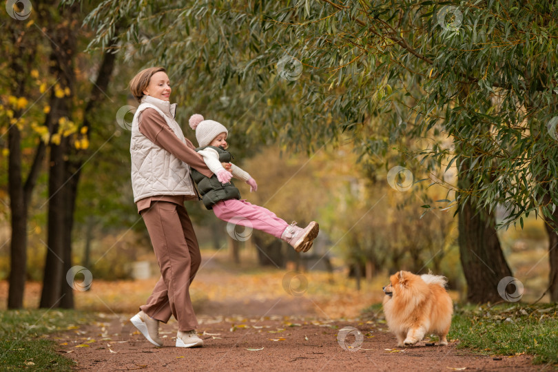 Скачать счастливая мать держит свою дочь на руках и кружится с ней по дорожке осеннего городского парка. фотосток Ozero