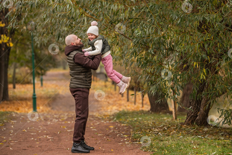 Скачать счастливый отец держит на руках свою дочь и хорошо проводит время в осеннем городском парке. фотосток Ozero