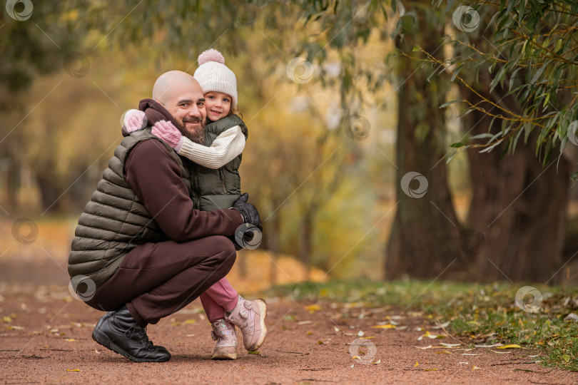 Скачать Маленькая дочь обнимает своего любящего отца во время прогулки по осеннему парку. фотосток Ozero