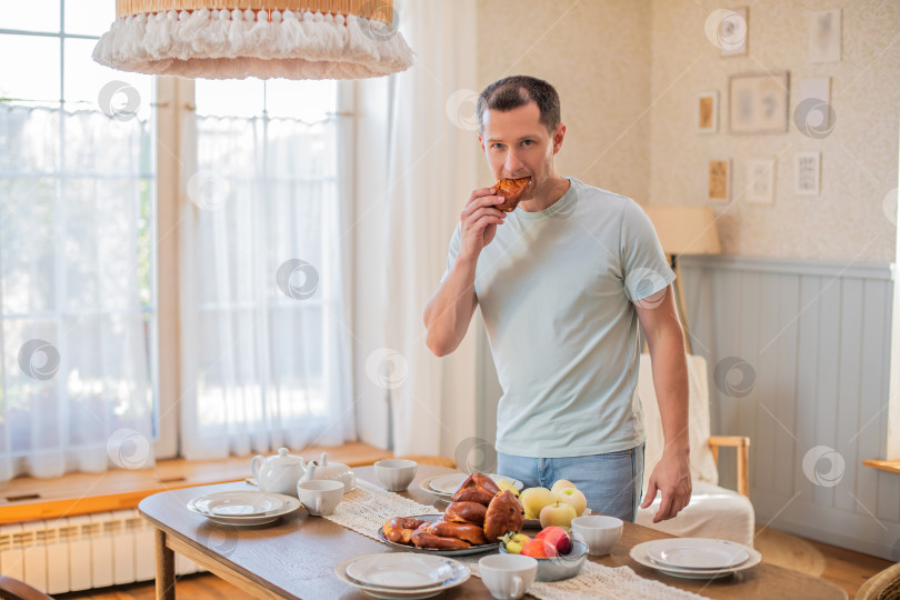 Скачать Молодой жизнерадостный мужчина на ходу берет со стола пирожки фотосток Ozero