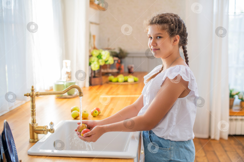 Скачать Молодая девушка моет яблоки на светлой кухне фотосток Ozero