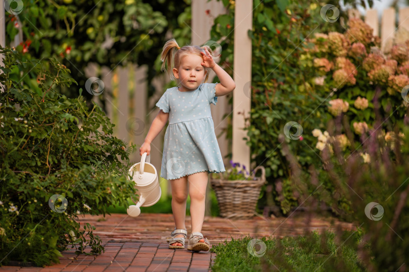 Скачать маленькая девочка в голубом платье идет по садовой дорожке с лейкой в руках. фотосток Ozero