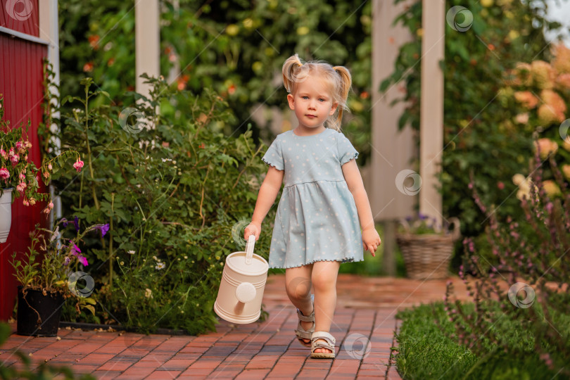 Скачать маленькая девочка в голубом платье идет по садовой дорожке с лейкой в руках. фотосток Ozero