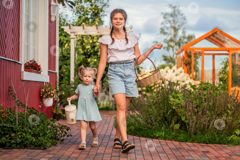 Скачать Сестры в летнем саду с корзинкой и лейкой в руках фотосток Ozero