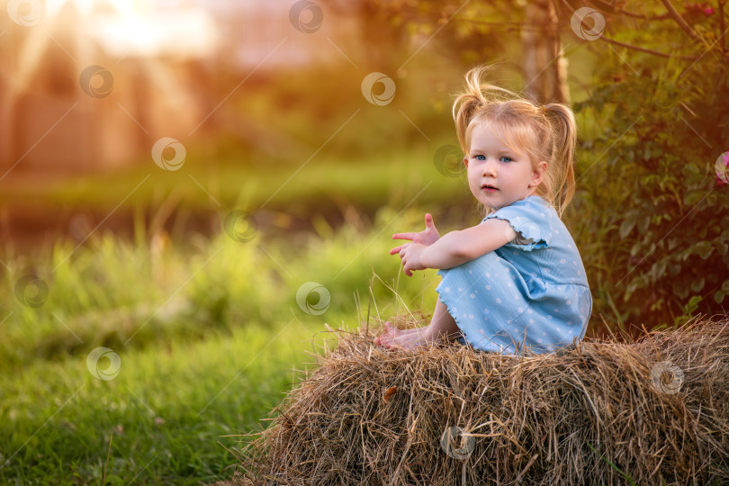 Скачать Маленькая девочка сидит на стогу сена в лучах заходящего солнца фотосток Ozero