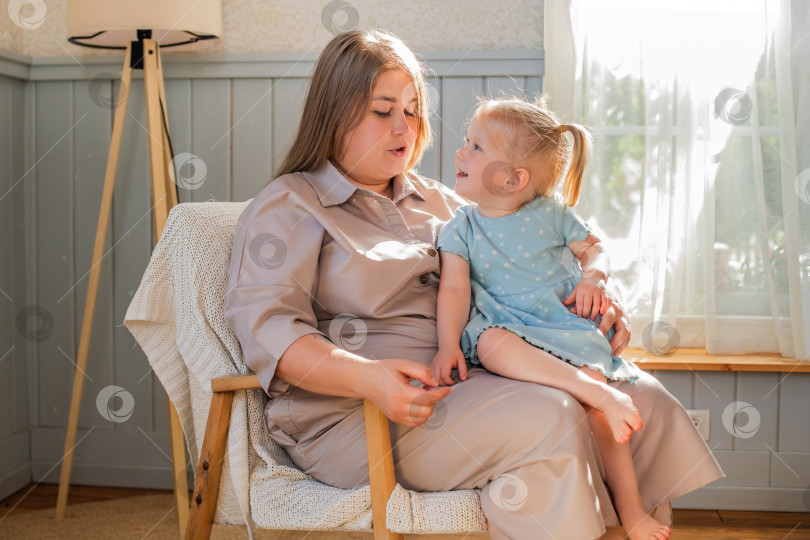 Скачать Мать счастливо играет со своей маленькой дочкой, сидя в кресле у окна. фотосток Ozero