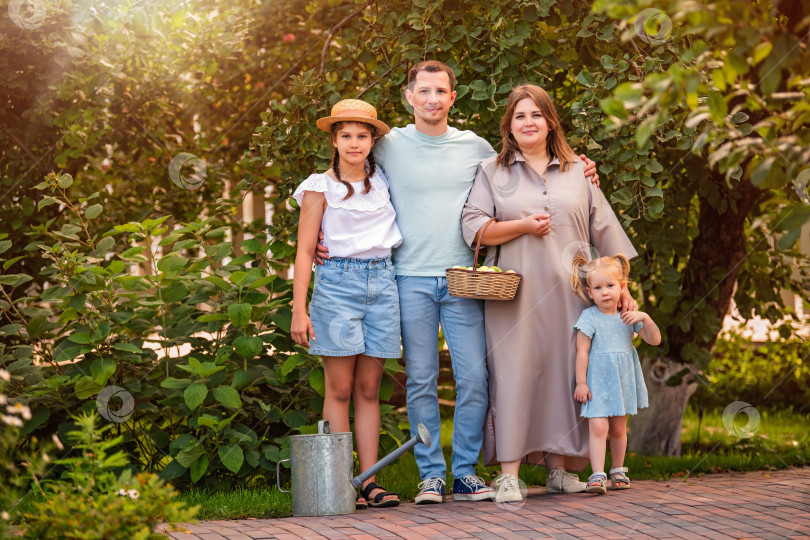 Скачать счастливая семья позирует в пышном летнем саду возле яблони с корзиной свежесобранных яблок. фотосток Ozero