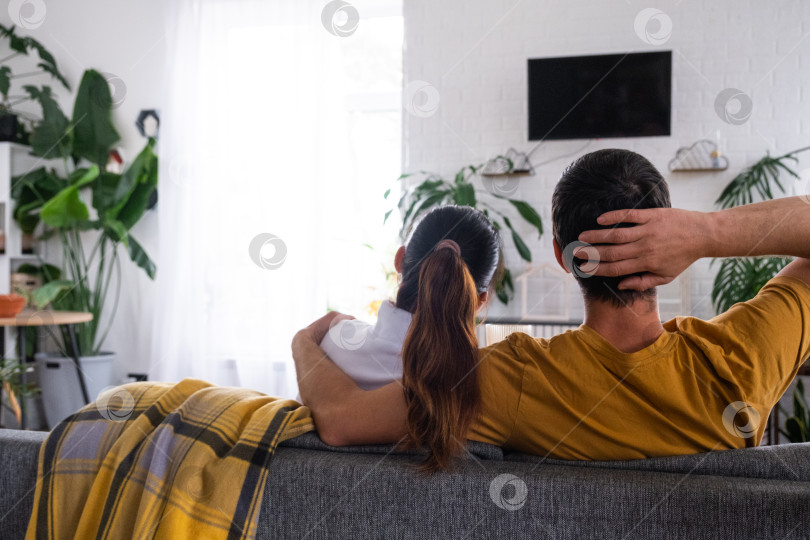 Скачать Мужчина и женщина дома в белом интерьере сидят на диване и смотрят телевизор, макет черного экрана. Домашний отдых, досуг, любовь, семья, свидание фотосток Ozero