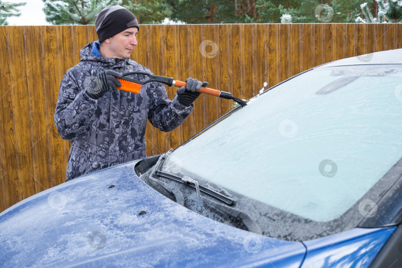 Скачать Мужчина очищает лобовое стекло автомобиля ото льда специальной щеткой фотосток Ozero