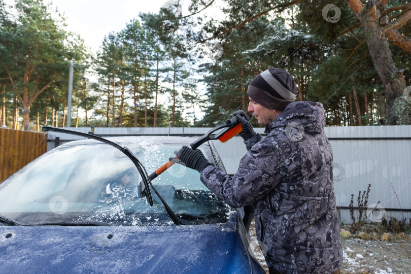 Скачать Мужчина очищает лобовое стекло автомобиля ото льда специальной щеткой фотосток Ozero