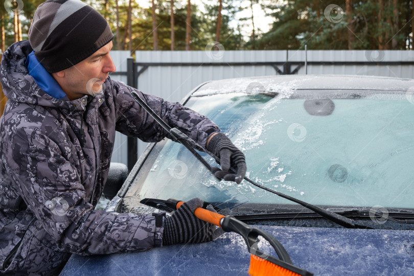 Скачать Мужчина очищает лобовое стекло автомобиля ото льда специальной щеткой фотосток Ozero