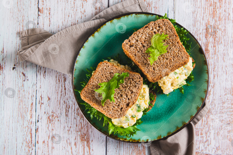 Скачать Аппетитный сэндвич с яичным салатом и авокадо на цельнозерновом хлебе крупным планом на тарелке, вид сверху фотосток Ozero