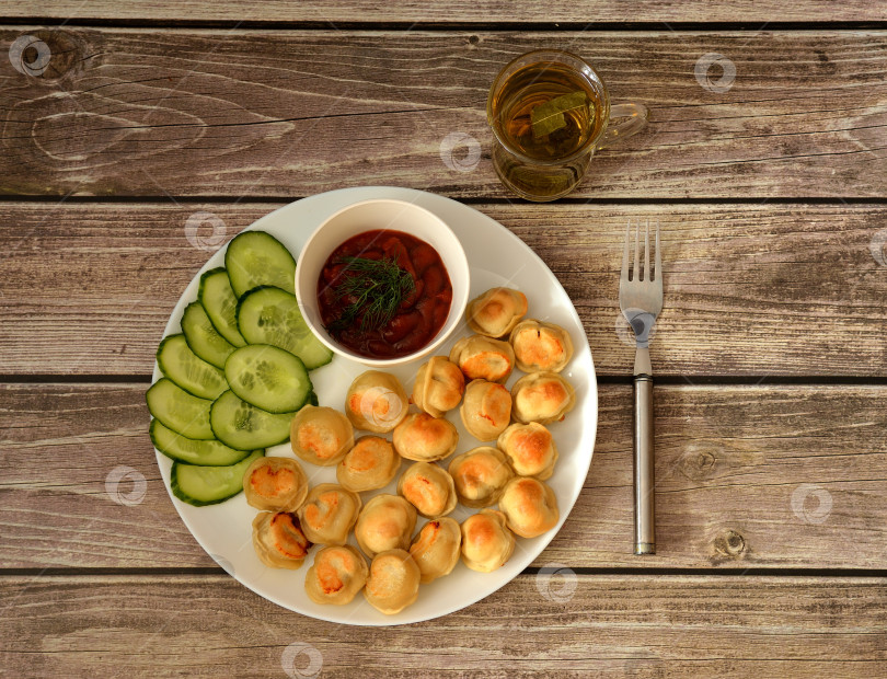 Скачать На деревянном столе стоит большая тарелка с жареными клецками, ломтиками свежего огурца и чашкой острого томатного соуса. фотосток Ozero