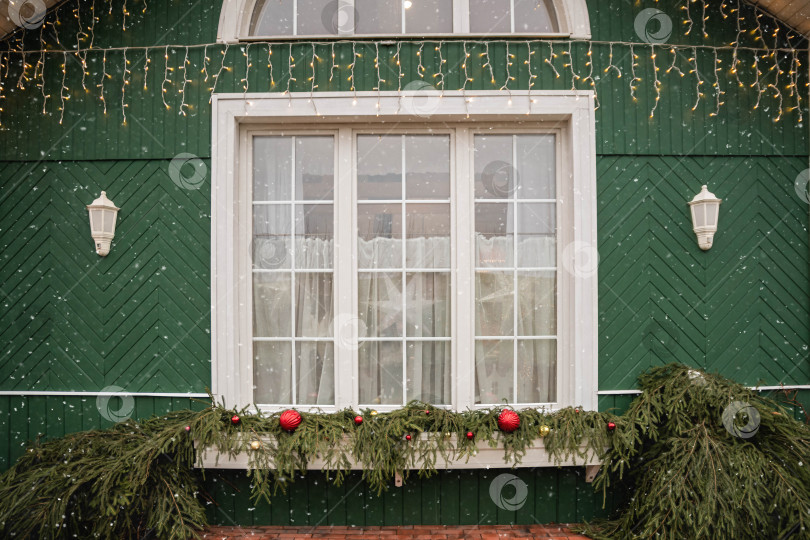 Скачать Большое окно в зеленом доме украшено праздничными рождественскими гирляндами и огнями. фотосток Ozero