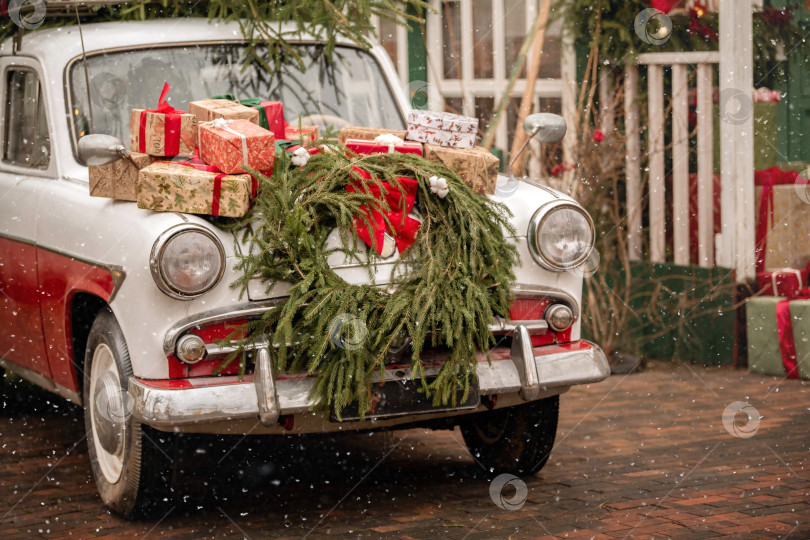 Скачать Винтажный автомобиль, украшенный праздничной гирляндой и подарочными коробками в снежный день. фотосток Ozero