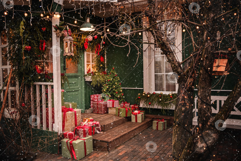 Скачать Уютное рождественское крыльцо дома, украшенное падающим снегом. фотосток Ozero