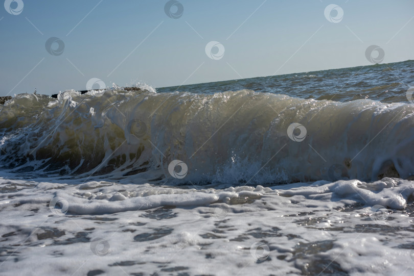 Скачать Большая волна, разбивающаяся о берег. Вода пенится и блестит на солнце. Видны брызги и пена. фотосток Ozero