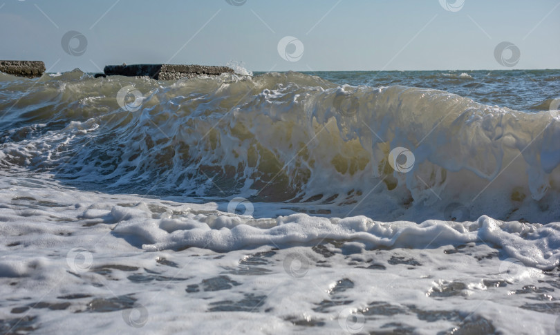Скачать Большая волна, разбивающаяся о берег. Вода пенится и блестит на солнце. Видны брызги и пена. фотосток Ozero