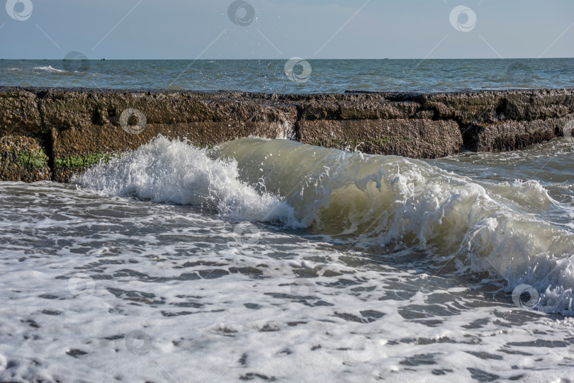 Скачать море с волнами, которые разбиваются о каменный волнорез. Вода пенистая и белая. фотосток Ozero