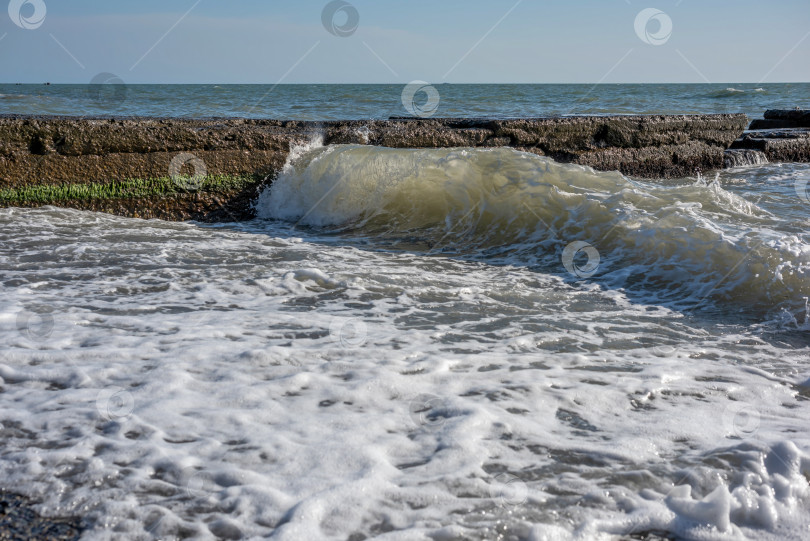 Скачать море с волнами, которые разбиваются о каменный волнорез. Вода пенистая и белая. фотосток Ozero