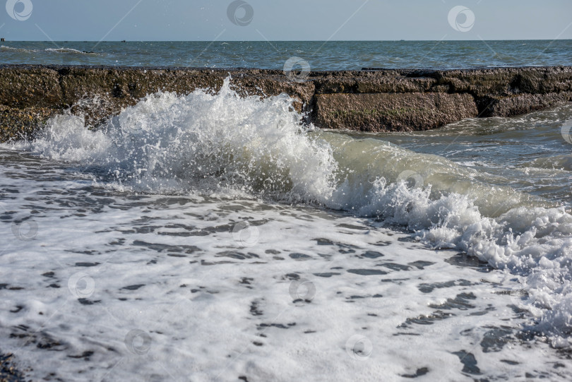Скачать море с волнами, которые разбиваются о каменный волнорез. Вода пенистая и белая. фотосток Ozero