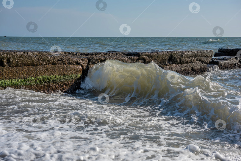 Скачать море с волнами, которые разбиваются о каменный волнорез. Вода пенистая и белая. фотосток Ozero