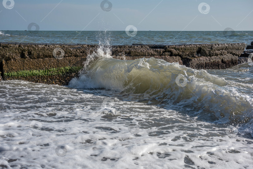 Скачать море с волнами, которые разбиваются о каменный волнорез. Вода пенистая и белая. фотосток Ozero