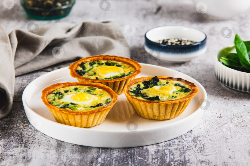 Скачать Запеченные тарталетки с перепелиными яйцами и свежим шпинатом на тарелке на столе фотосток Ozero