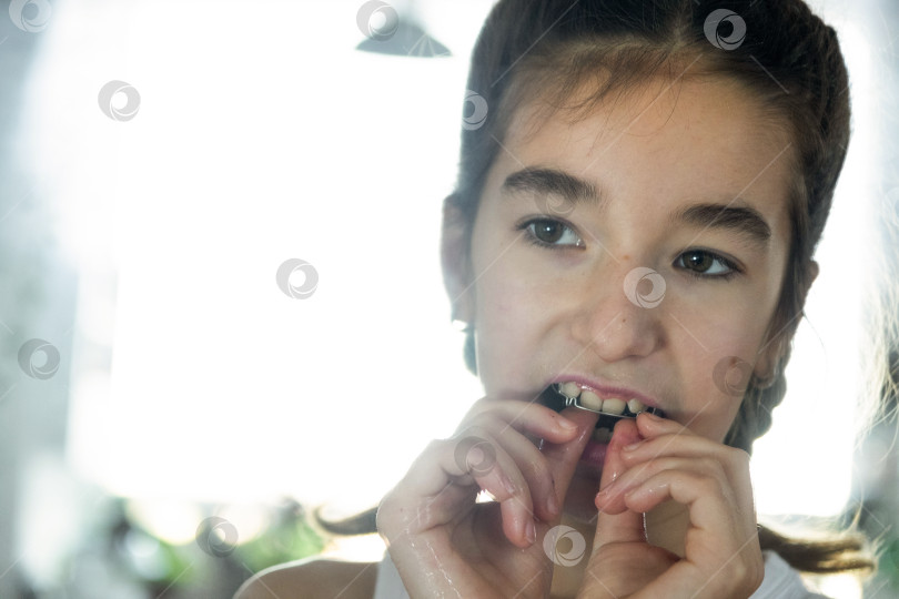 Скачать Девушка вставляет пластинки для коррекции зубов перед зеркалом, утренняя гигиена, брекеты фотосток Ozero