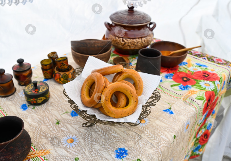 Скачать Славянский стол с рогаликами, глиняными горшочками и деревянной посудой на скатерти в цветочек. Традиционный русский народный стиль и деревенская культура ручной работы. фотосток Ozero
